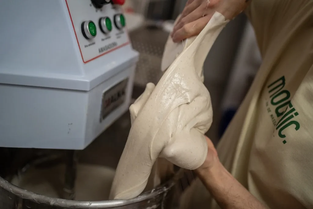 Mans comprovant l’elasticitat de la massa al costat de la pastadora